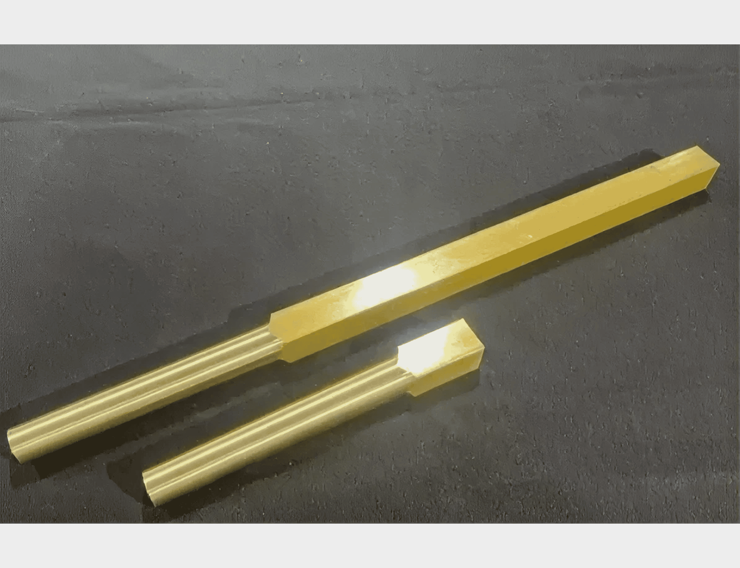 Two golden metal rods on black surface.